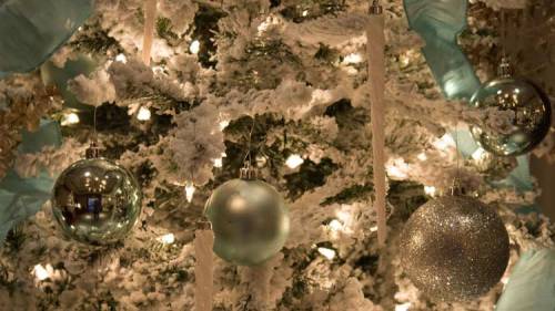 A decorated Christmas tree with white lights, snowy branches, and blue and silver ornaments.