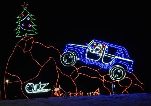 A brightly lit display featuring a Jeep with a Santa figure, next to a decorated Christmas tree and festive lights.