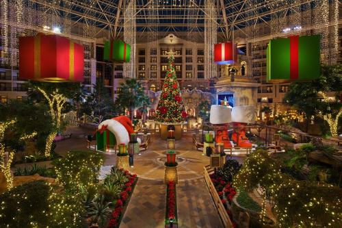A festive indoor space decorated for Christmas, featuring a large tree, oversized gifts, and twinkling lights.
