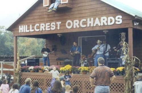 A band performs on stage at Hillcrest Orchards, with an audience enjoying the music and colorful flowers in front.