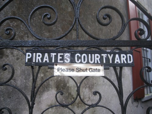Sign on a wrought iron gate reading "Pirates Courtyard" with a smaller sign saying "Please Shut Gate."