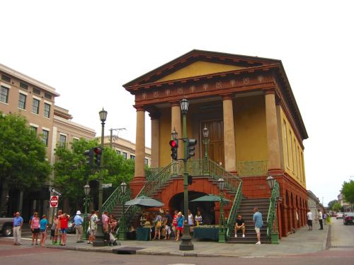Historic building with columns and stairs, surrounded by people and trees, in an urban setting. Traffic lights visible.