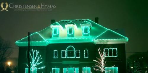 A house decorated with green and blue lights, illuminated against a dark night sky.