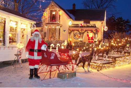 A festive scene with Santa by a decorated sleigh, surrounded by lights and holiday decorations on a snowy evening.