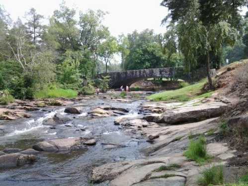 A serene river scene with a stone bridge in the background, surrounded by lush greenery and rocky banks.