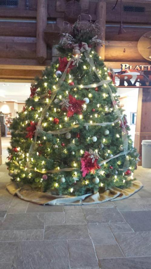 A beautifully decorated Christmas tree with lights, ornaments, and ribbons, set in a cozy indoor space.