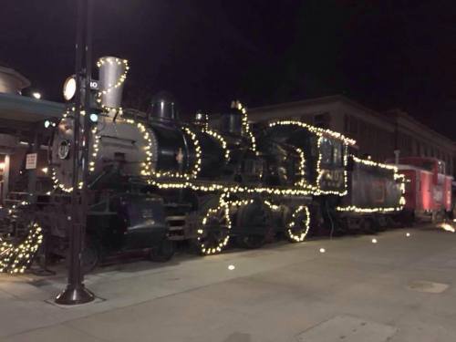 A vintage steam train decorated with string lights, parked at a station at night.