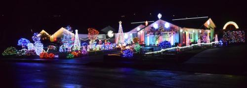 A brightly lit house decorated with colorful Christmas lights and festive displays, set against a dark night sky.