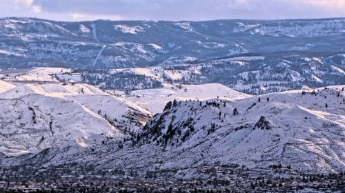 Snow-covered mountains and hills under a cloudy sky, with a valley visible in the foreground.