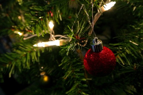 A close-up of a Christmas tree with a shiny red ornament and warm white lights in the background.