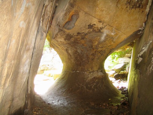 A natural rock formation with a curved opening, revealing a glimpse of greenery and water beyond.