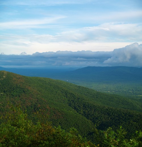 A panoramic view of lush green mountains under a cloudy sky, with distant hills fading into the horizon.