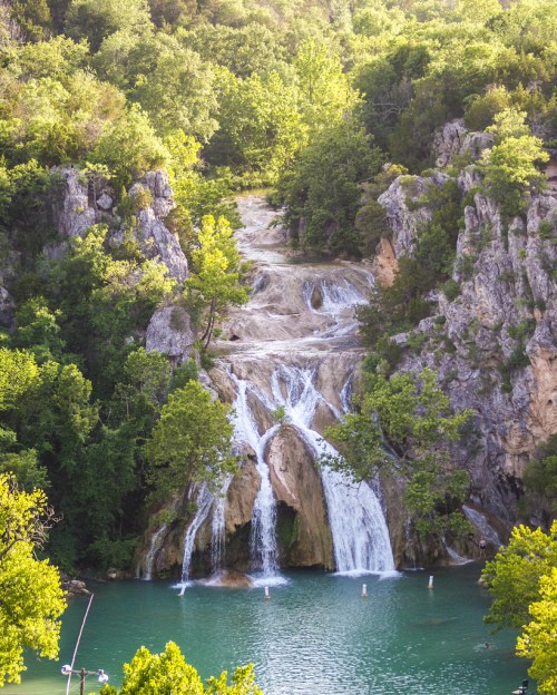 A serene waterfall cascading down rocky cliffs into a tranquil turquoise pool, surrounded by lush green trees.