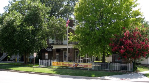 A brick building with trees and a sign promoting mobile banking, featuring an American flag in front.