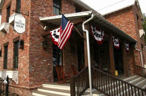 Exterior of a brick building named "The Meeting House," featuring an American flag and patriotic decorations.