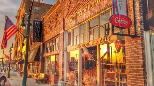 A vibrant street scene at sunset featuring a gallery, shops, and American flags on a brick building.