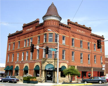 Historic red brick building with a turret, featuring green awnings and decorative architectural details.