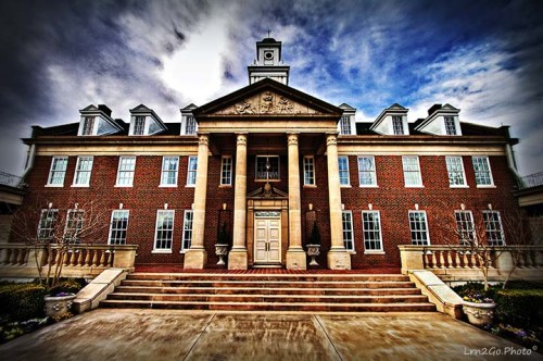 Historic brick building with columns, a clock tower, and a dramatic sky, featuring a grand entrance and landscaped steps.