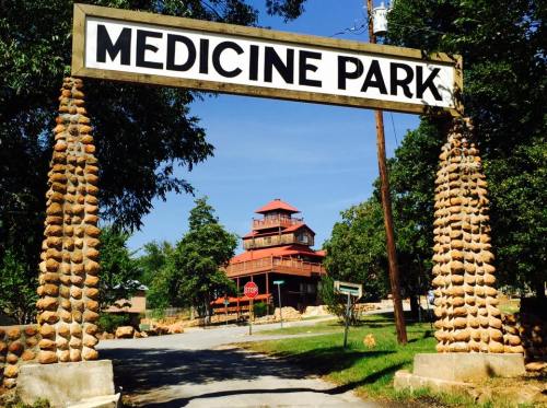 Sign for Medicine Park with a stone archway and a building in the background under a clear blue sky.