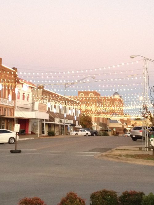 A charming street scene at dusk, adorned with string lights illuminating buildings and a quiet road.