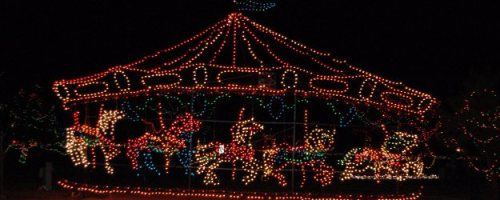 A brightly lit carousel adorned with colorful lights, set against a dark night sky.