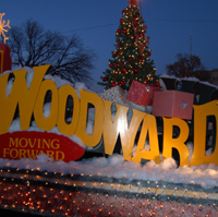 A festive display featuring the word "Woodward" with holiday decorations, snow, and a Christmas tree in the background.