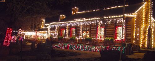 A beautifully lit log cabin adorned with colorful Christmas lights at night.