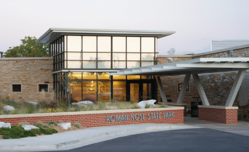 Modern visitor center of Roman Nose State Park with large windows and stone exterior, surrounded by landscaping.