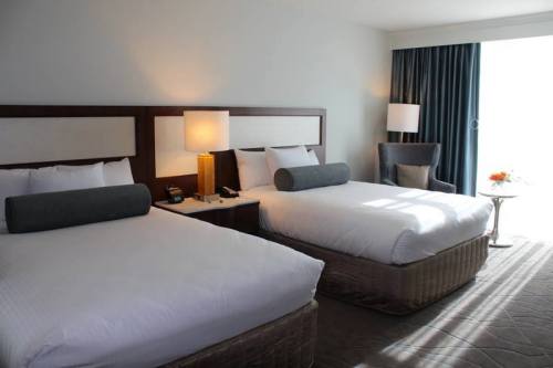 A modern hotel room featuring two beds, a chair, and a small table by a window with natural light.