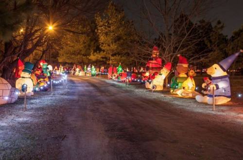 A festive pathway lined with colorful inflatable holiday decorations, including snowmen and Christmas trees, at night.