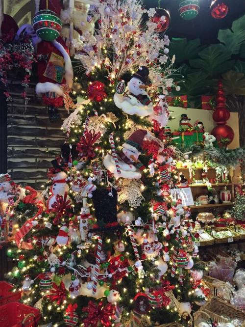 A festive Christmas tree adorned with snowmen, candy canes, and red and white decorations, surrounded by holiday decor.
