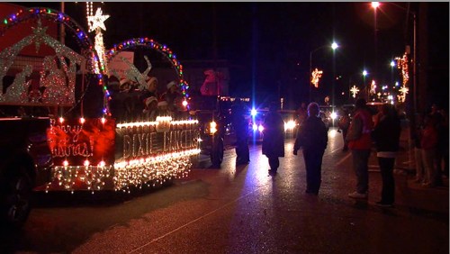 A festive parade float decorated with lights, passing by spectators on a street at night.