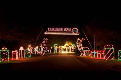Colorful holiday lights create a festive entrance to a decorated town, featuring gifts and cheerful holiday figures.
