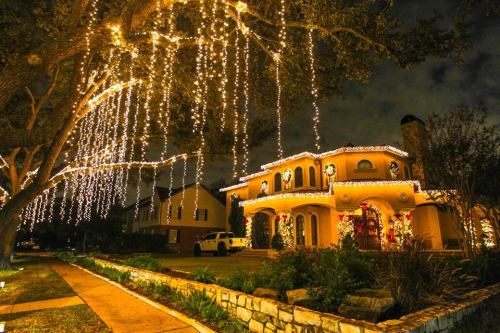 A beautifully decorated house with festive lights hanging from trees, creating a warm holiday atmosphere at night.