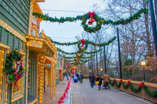 A festive walkway adorned with Christmas lights, wreaths, and decorations, with people strolling in a winter setting.