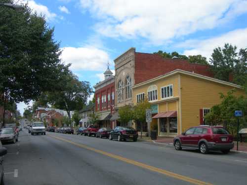 A charming small town street lined with shops and parked cars under a blue sky with scattered clouds.