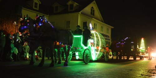 A festive night scene with illuminated horse-drawn carriages and people enjoying a holiday parade.