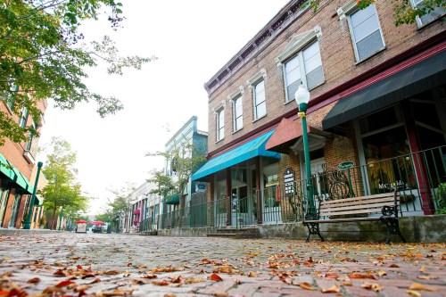 A quaint street lined with brick buildings, colorful awnings, and fallen leaves, creating a charming, peaceful atmosphere.