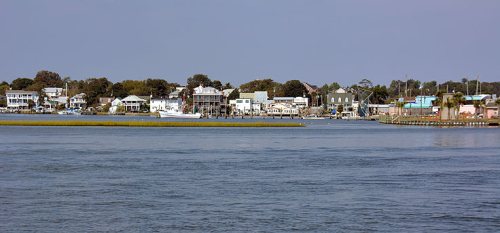 A scenic view of a waterfront town with buildings lining the shore and boats in the water under a clear sky.