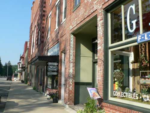 A charming brick building with storefronts, featuring a closed sign and a collectibles shop, along a quiet street.