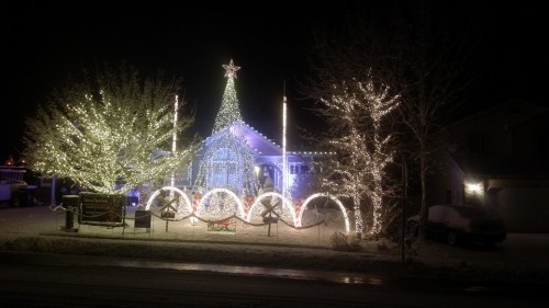 A beautifully decorated house with a large Christmas tree and bright lights, surrounded by snow at night.