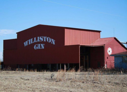 Red building with "Williston Gin" painted on the side, set against a clear blue sky and dry grass in the foreground.