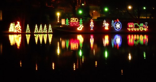 Colorful holiday lights reflecting on water, featuring trees, a train, and festive decorations.