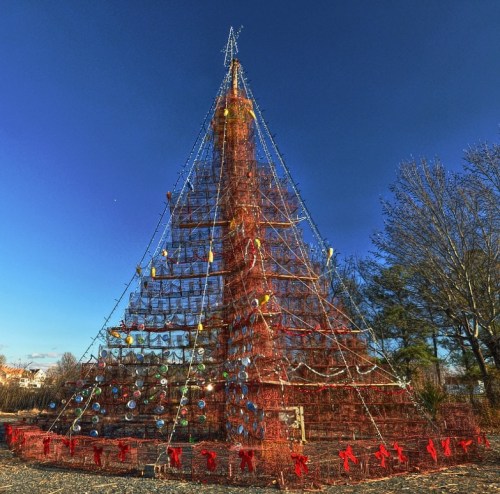 A large, decorated Christmas tree made of lights and ornaments against a clear blue sky.