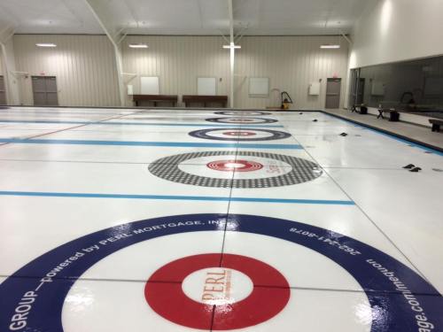 A curling rink with multiple target circles on the ice, featuring a clean, well-maintained interior.