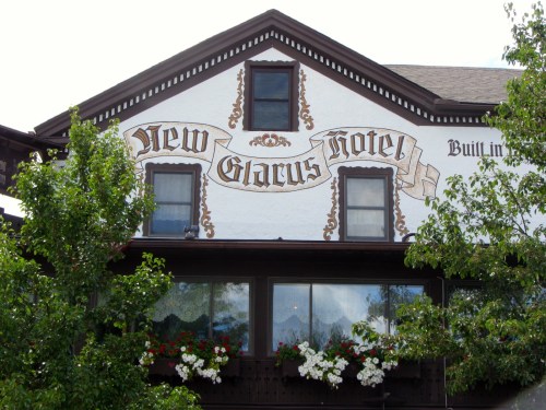 Historic New Glarus Hotel building with decorative signage and flower boxes under a clear sky.