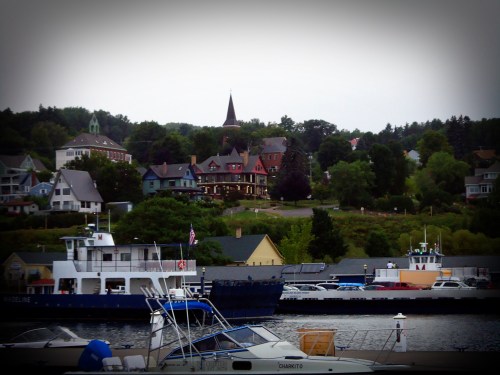 A scenic waterfront view featuring boats and colorful houses on a hillside, with a church steeple in the background.
