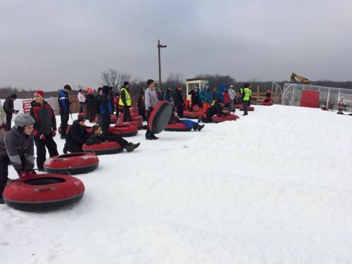 A group of people sitting on snow tubes at a snowy hill, ready to go tubing on a cloudy day.