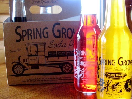 A cardboard soda carrier with three colorful bottles labeled "Spring Grove Soda Pop" in various flavors.