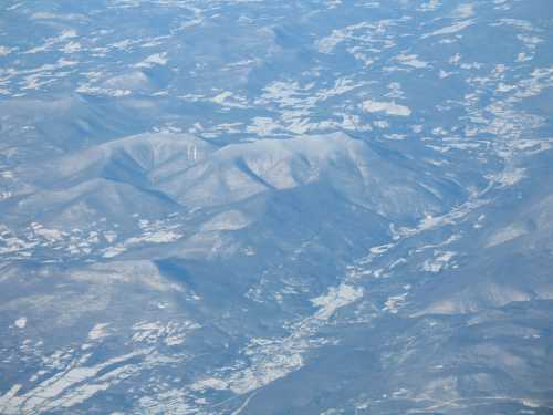 Aerial view of snow-covered mountains and valleys under a clear blue sky.